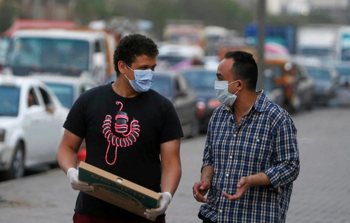 Men wearing face masks walk along a street before curfew in Shubra El Kheima, Al Qalyubia Governorate, north of Cairo. (REUTERS)