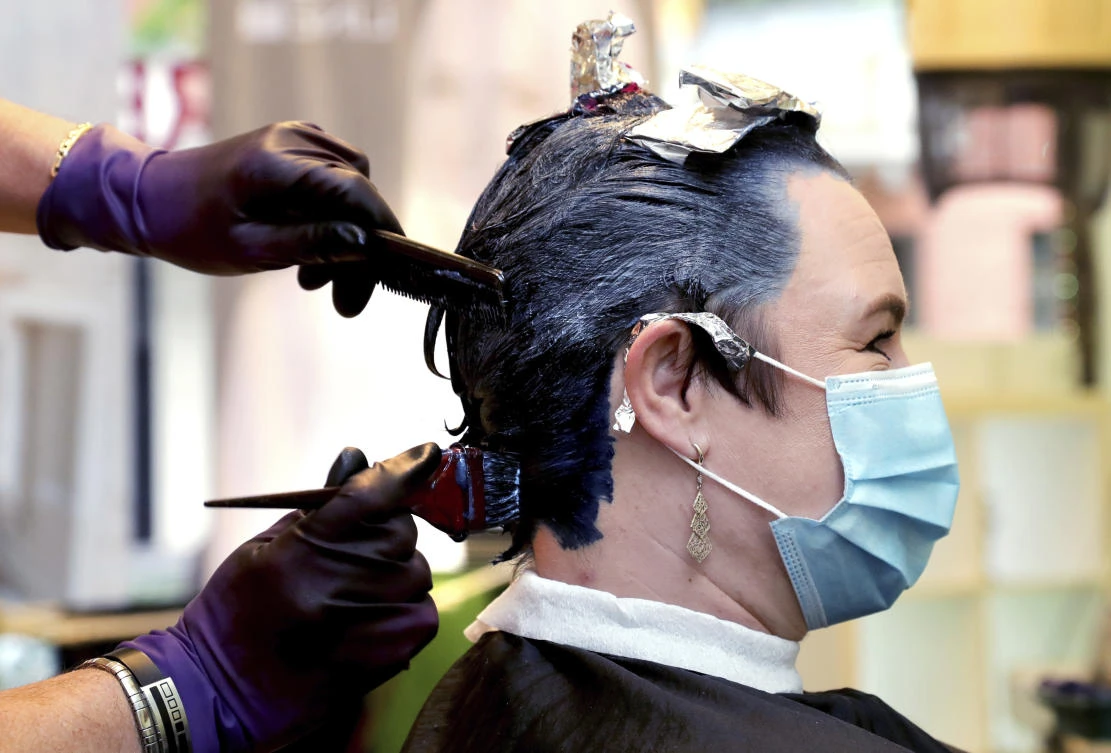 A hairdresser tints and cuts hair of a customer in his hairdressing salon in Berlin, Germany, Monday, May 4, 2020. After weeks of a lockdown due to the new coronavirus outbreak German hairdresser reopend their shops on Monday. (AP Photo/Michael Sohn)