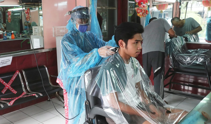 A barber in Jakarta wearing a face mask to protect against COVID-19 gives a customer a haircut. (AP)