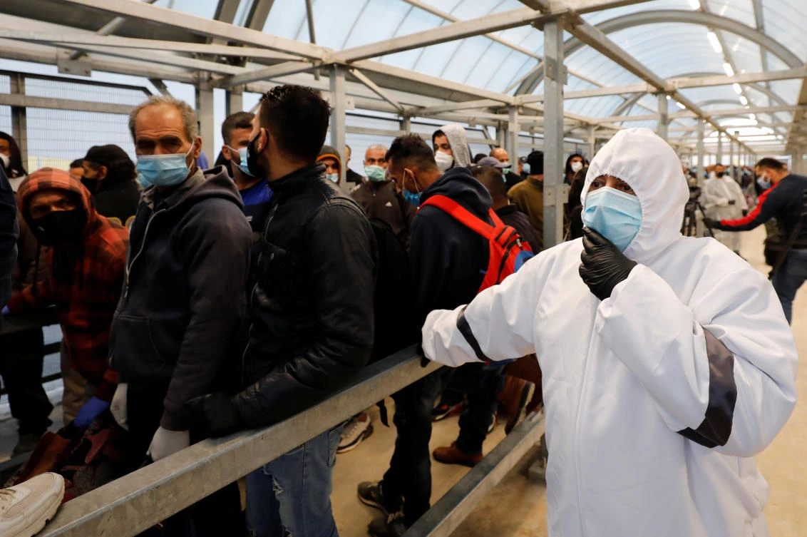 A health worker watches as Palestinian laborers head to work in Israel through a checkpoint near Hebron amid concerns about the spread of the coronavirus. (Reuters)