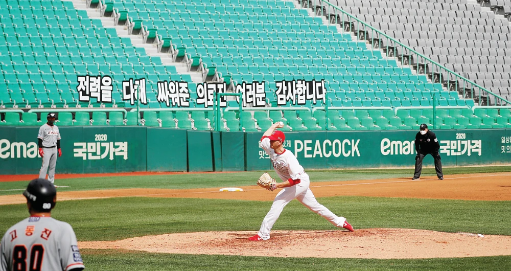 A banner thanking medical workers is seen while SK Wyverns’ Nick Kingham throws the ball during the match against Hanwha Eagles on Tuesday. The new baseball season began without fans watching. (Reuters)