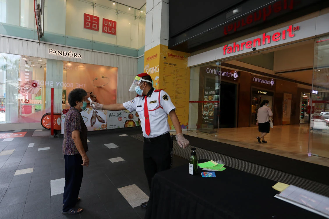 A security guard checks a customer’s temperature at a mall entrance as Malaysia reopens a majority of businesses on May 4, 2020. (Reuters)