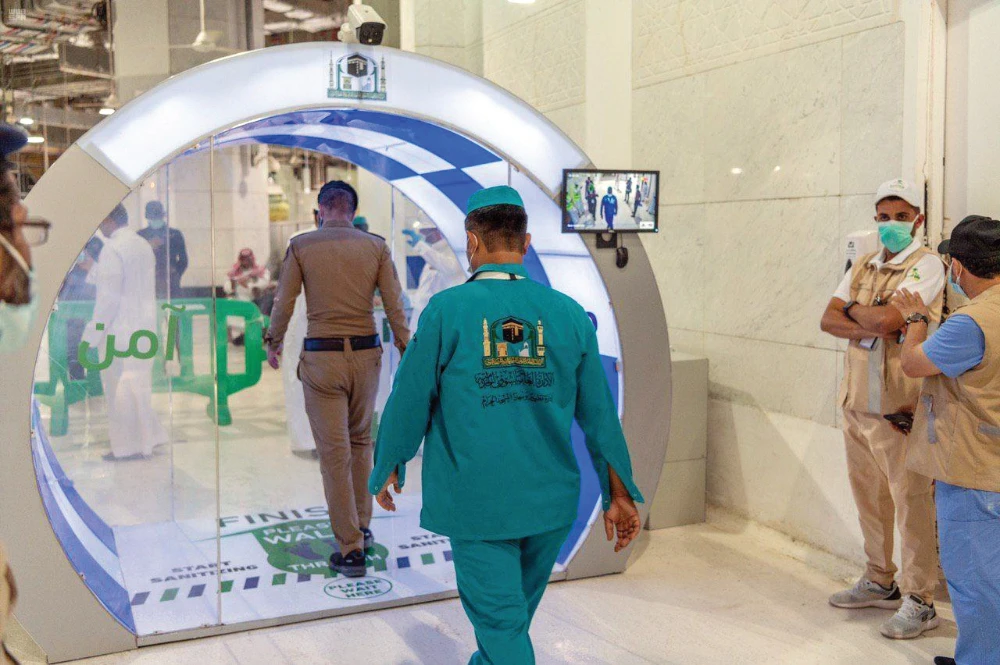 A police officer and a worker pass through a gate equipped with automatic sanitizers at the Makkah Grand Mosque on Thursday. (SPA)