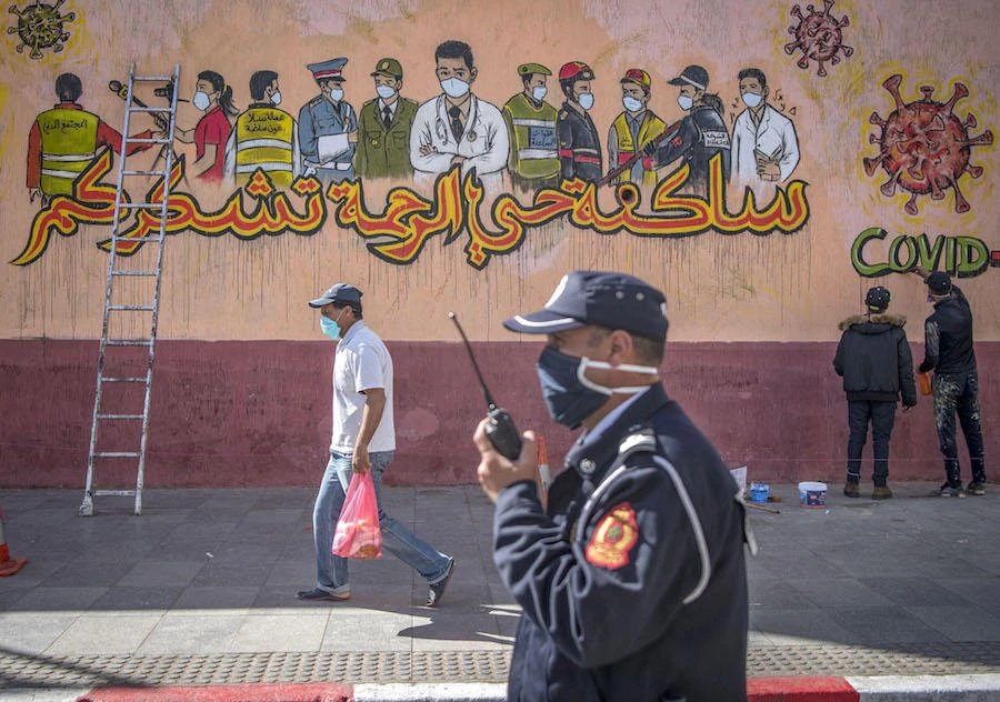 A Moroccan policeman walks past artists working on a mural thanking essential workers amid the COVID-19 pandemic, in the city of Sale north of the capital, on April 26, 2020. (AFP)