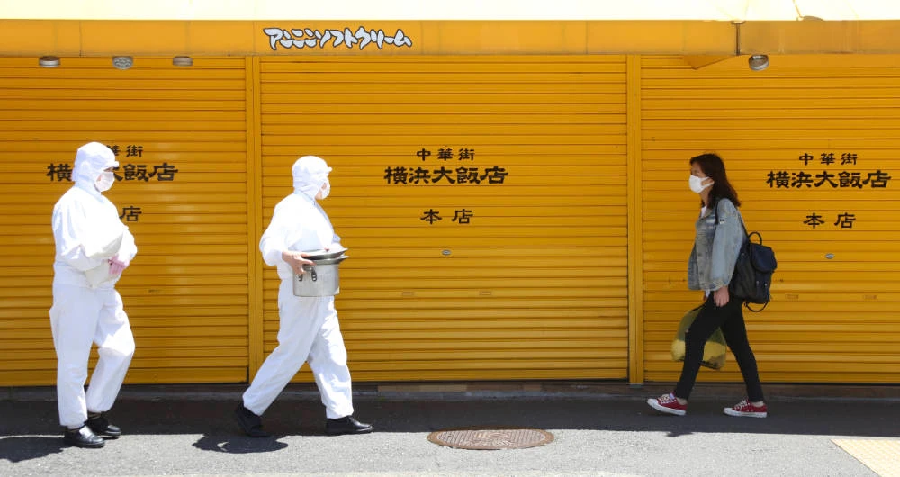 Employees of a restaurant wearing protective suits against the spread of the new coronavirus walk through China Town in Yokohama, near Tokyo, Friday, May 8, 2020. (AP)