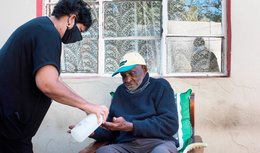 Fredie Blom (R) is given hand sanitiser by one of his wife's daughters, as a preventive measure against the spread of the COVID-19 coronavirus, as he celebrates his 116th birthday at his home in Delft, near Cape Town, on May 8, 2020. (AFP)