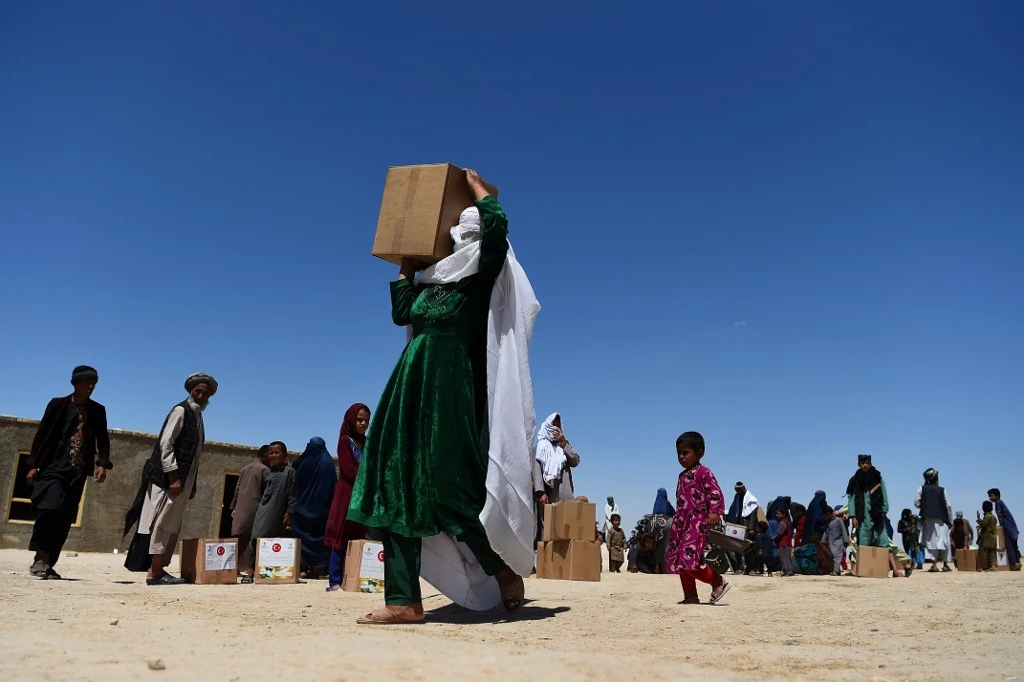 A woman carries free aid over her shoulders distributed on May 3, 2020 in a refugee camp on the outskirts of Mazar-i-Sharif in Afghanistan. (AFP file photo)