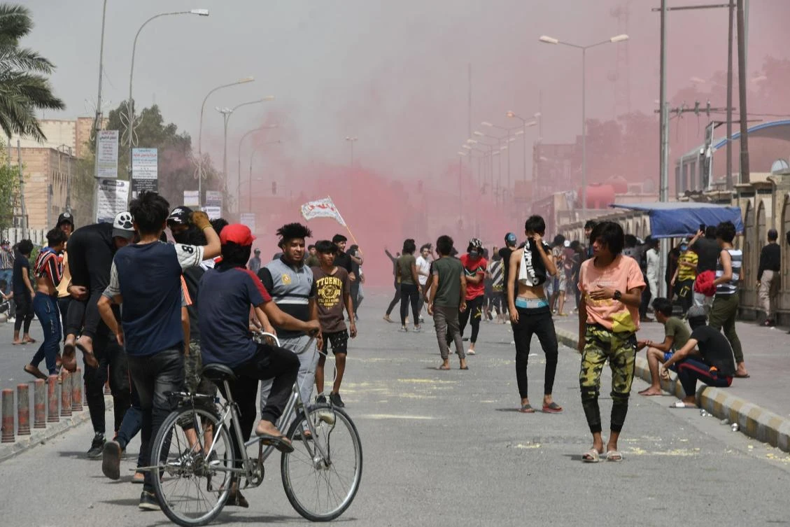 Iraqi protesters flee smoke grenades fired by security forces amid clashes following an anti-government demonstration in the Iraqi city Nasiriyah in Dhi Qar province, on May 10, 2020. (AFP)