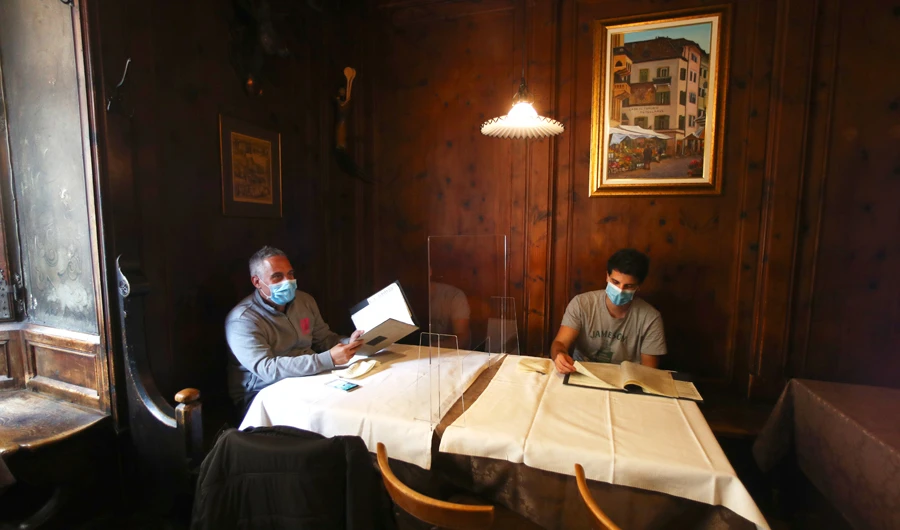 People wear masks to protect against the coronavirus as they sit next to a protective plastic window in a restaurant in Bozen, Italy, on Monday. (AP)