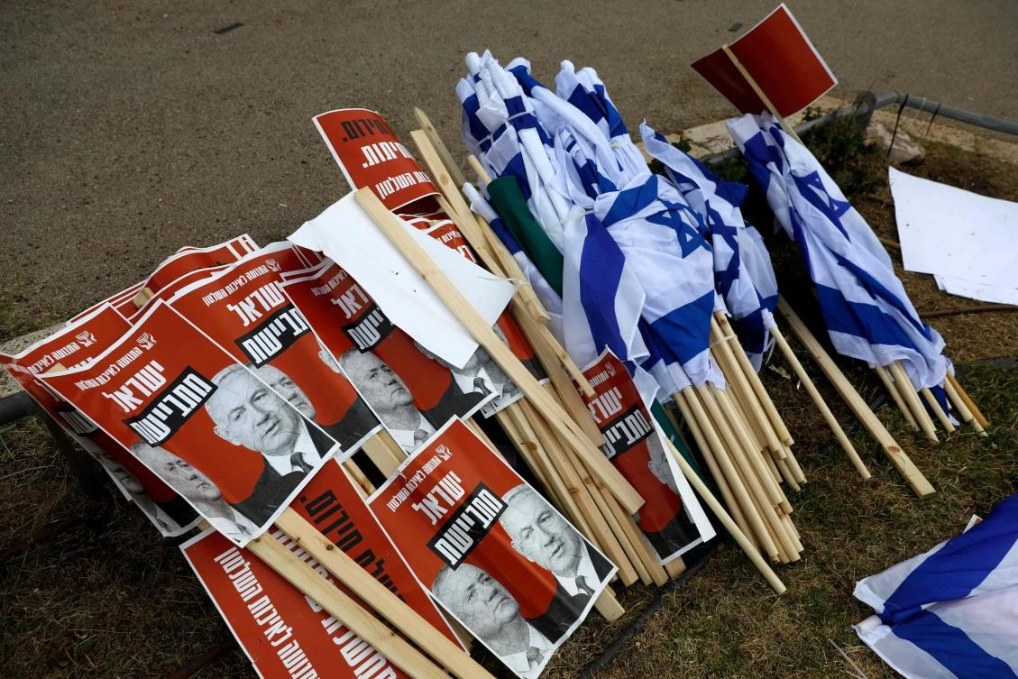 Israeli flags lie on the ground alongside signs showing the faces of Israeli Prime Minister Benjamin Netanyahu (R) and ex-rival Benny Gantz (L) with a caption in Hebrew reading "Israeli ashamed", during a demonstration protesting against the new Israeli government expected to be sworn-in later after nearly 18 months of political gridlock, outside the Knesset (Israel's parliament) in Jerusalem, on May 14, 2020. (AFP)