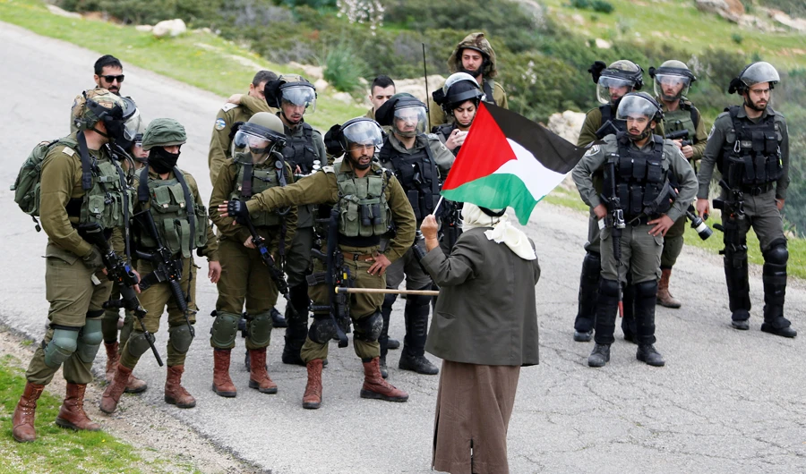 A demonstrator holding a Palestinian flag stands in front of Israeli forces during a protest against Israeli settlements and the U.S. President Donald Trump's Middle East peace plan, in Jordan Valley in the Israeli-occupied West Bank February 25, 2020. (REUTERS)