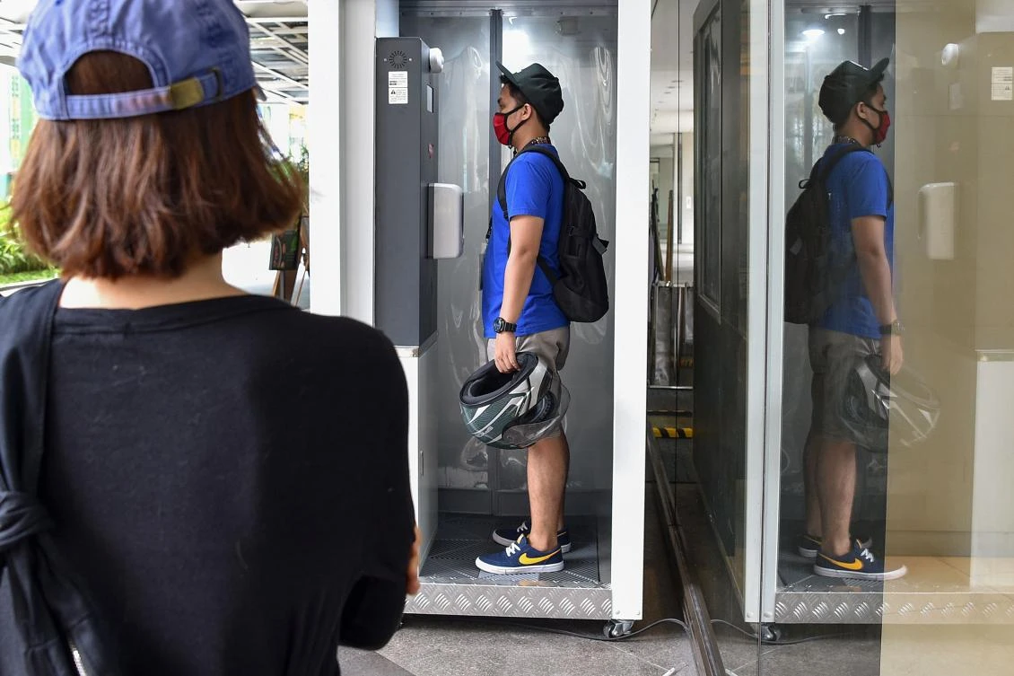 A shopper waits for her turn while another stands inside a temperature and disinfection channel installed at the entrance of a shopping mall as the Philippine capital began to partially re-open businesses on May 16, 2020. (AFP)