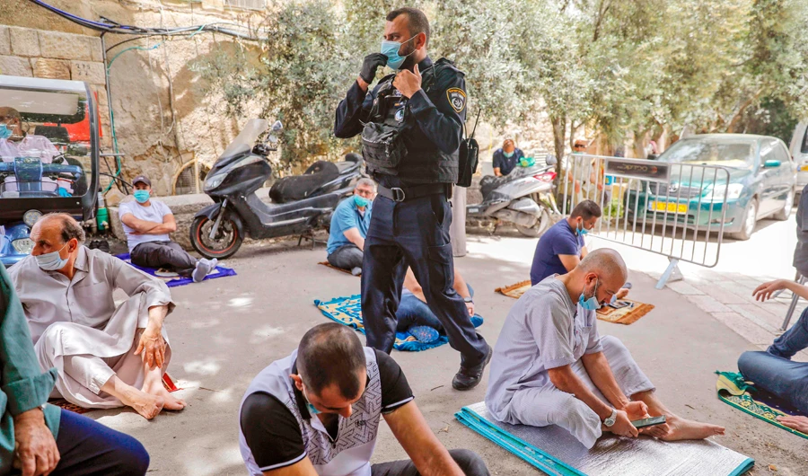 An Israeli soldier walks among Palestinian worshippers as they pray outside the closed Al-Aqsa Mosque compound in Jerusalem. (AFP)