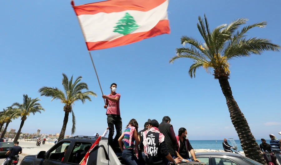 Wearing a mask for protection against COVID-19 disease, a demonstrator waves a Lebanese flag during a protest against the growing economic hardship in Tyre. (Reuters/File)