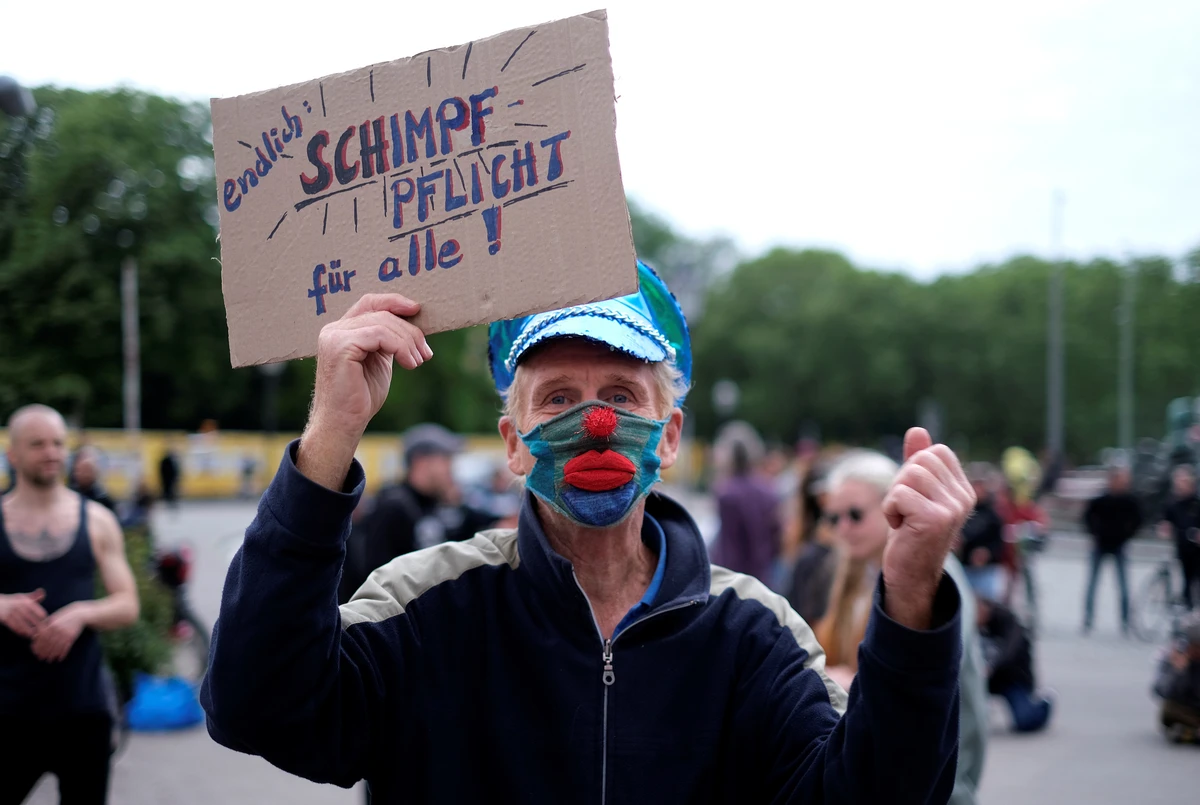 A man wearing a face mask shows a signs reading "finally: compulsory grumbling for all!" during a protest against the government's coronavirus restrictions. (REUTERS)