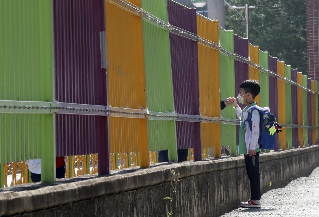 South Korean schools have been re-opening in phases in a process that is continuing nationwide. A pupil holds his mother’s hand through the fence of Ochi Elementary School in Gwangju. (Yonhap via AP)