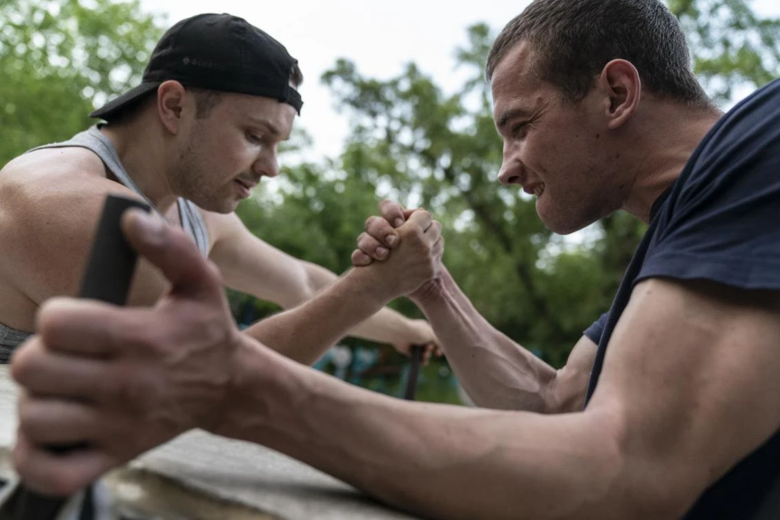 In this photo taken on Monday, June 8, 2020, two men compete in arm wrestling in the outdoors gym on the Dolobetskiy island on the Dnipro River in Kyiv, Ukraine. Relishing an opportunity to do exercise after a long lockdown, hundreds of Kyiv residents flock to an improvised outdoor workout on an island facing the Ukrainian capital. The Kachalka gym on the Dolobetskiy island on the Dnipro river has enjoyed broad popularity ever since it opened in 1966. (AP Photo/Evgeniy Maloletka)