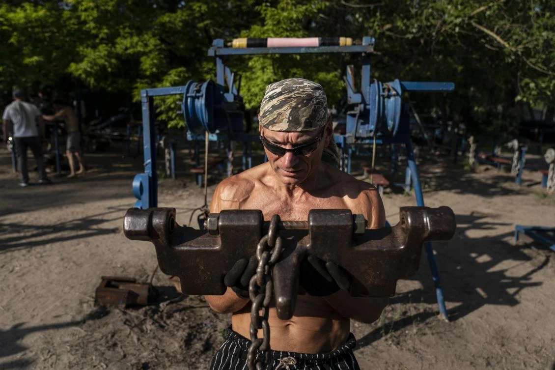 In this photo taken on Saturday, June 6, 2020, Andriy Demyanchenko, 55, trains uses a part of the tracks of the tank in the outdoors gym on the Dolobetskiy island on the Dnipro River in Kyiv, Ukraine. Relishing an opportunity to do exercise after a long lockdown, hundreds of Kyiv residents flock to an improvised outdoor workout on an island facing the Ukrainian capital. The Kachalka gym on the Dolobetskiy island on the Dnipro river has enjoyed broad popularity ever since it opened in 1966. (AP Photo/Evgeniy Maloletka)