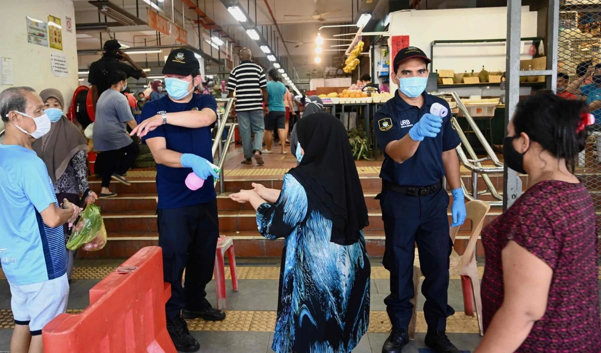 Security personnel check the temperatures of people entering a market, while enforcing social distancing, in Penang on May 29, 2020 as Malaysia eases its partial lockdown due to the COVID-19 novel coronavirus. (AFP)
