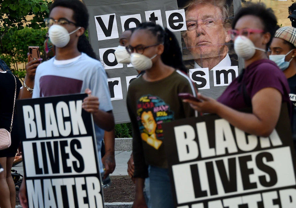 Demonstrators holding Black Lives Matter signs stand by a sign calling to vote out racism with a picture of President Donald Trump, during a peaceful protest against police brutality and the death of George Floyd, on June 7, 2020 in Washington, DC. (AFP / Olivier Douliery)