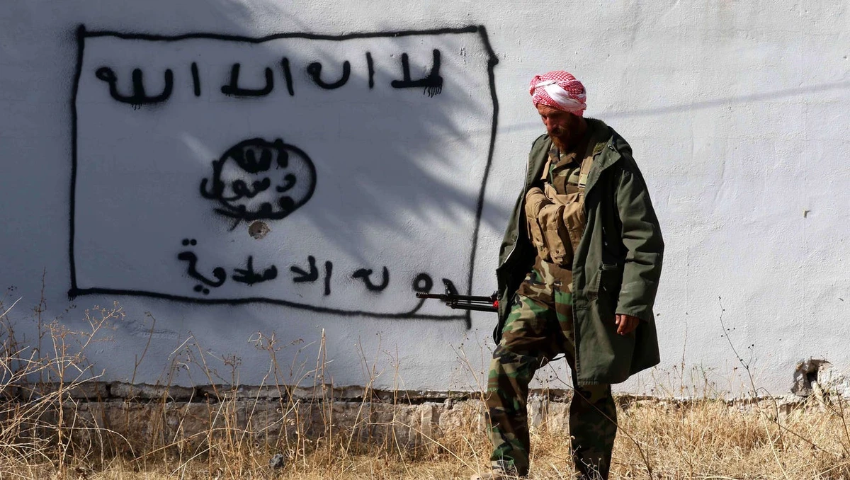 A Kurdish fighter walks by a wall bearing a drawing of the flag of Daesh group in the northern Iraqi town of Sinjar, in the Nineveh Province, on November 13, 2015. (AFP/ File photo)