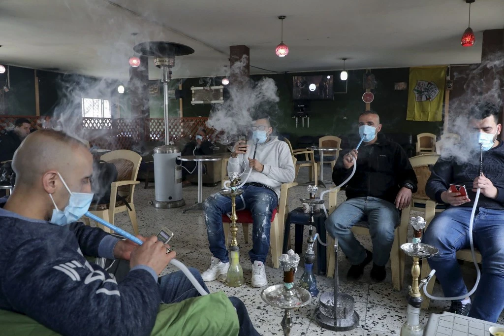 Palestinian men smoke the shisha (waterpipe) while wearing protective masks at a coffee shop in the West Bank city of Hebron, on March 7, 2020, amid fears of the spread of the novel coronavirus. (File/AFP)