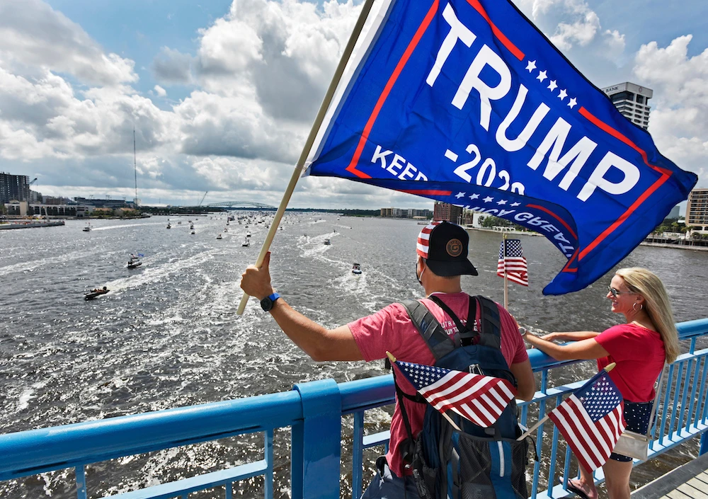 Brian Masotti, left, and Tracey Warren wave flags at the hundreds of boats idling on the St. Johns River during a rally Sunday, June 14, 2020, in Jacksonville, Florida, celebrating President Donald Trump’s birthday. (Will Dickey/The Florida Times-Union via AP)