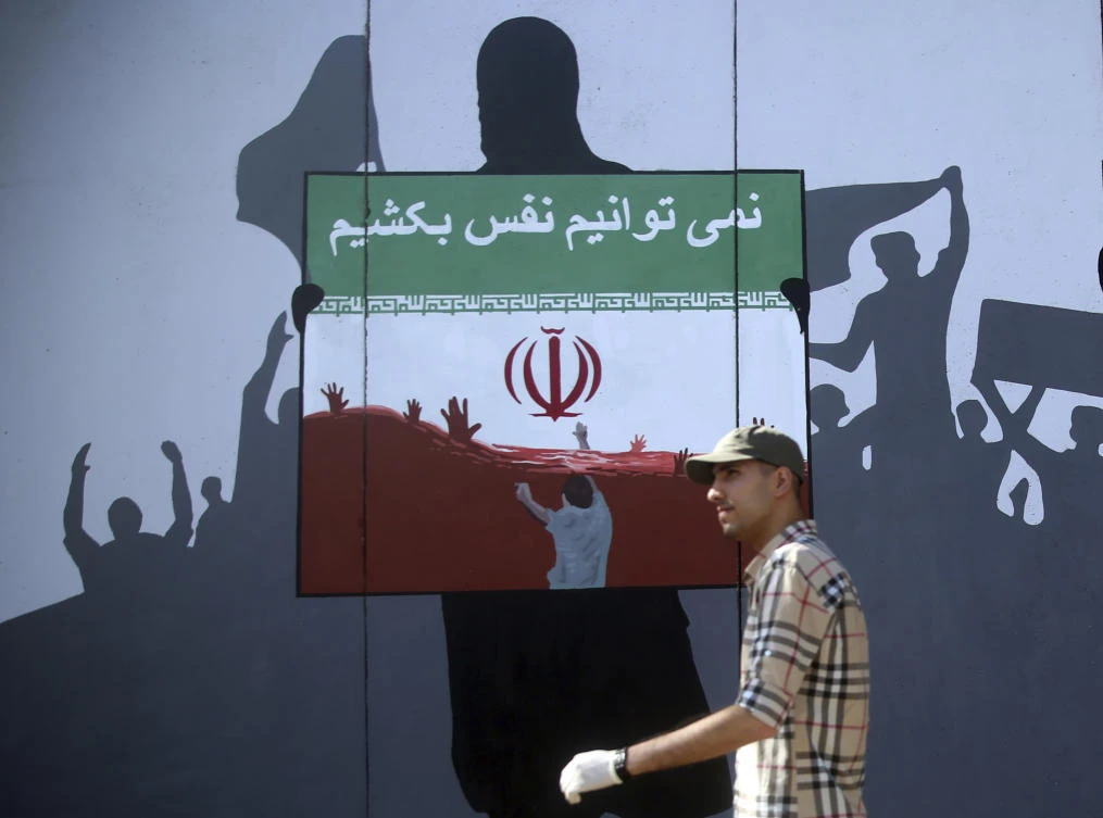 A man walks past a painting on a wall with writing in the Dari Language reading "We cannot breath" during a protest themed Killings of Afghans in Iran in Kabul, Afghanistan, Monday, June 15, 2020. (AP)
