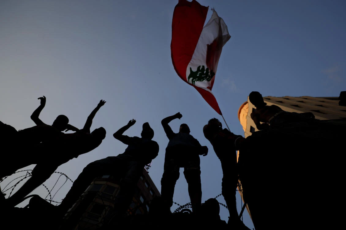 Anti-government protesters wave a Lebanese national flag while standing on a concrete wall that was installed by the authorities to block a road leading to the parliament building during ongoing protests against the Lebanese government in Beirut, Lebanon, Sunday, June 14, 2020. (AP)