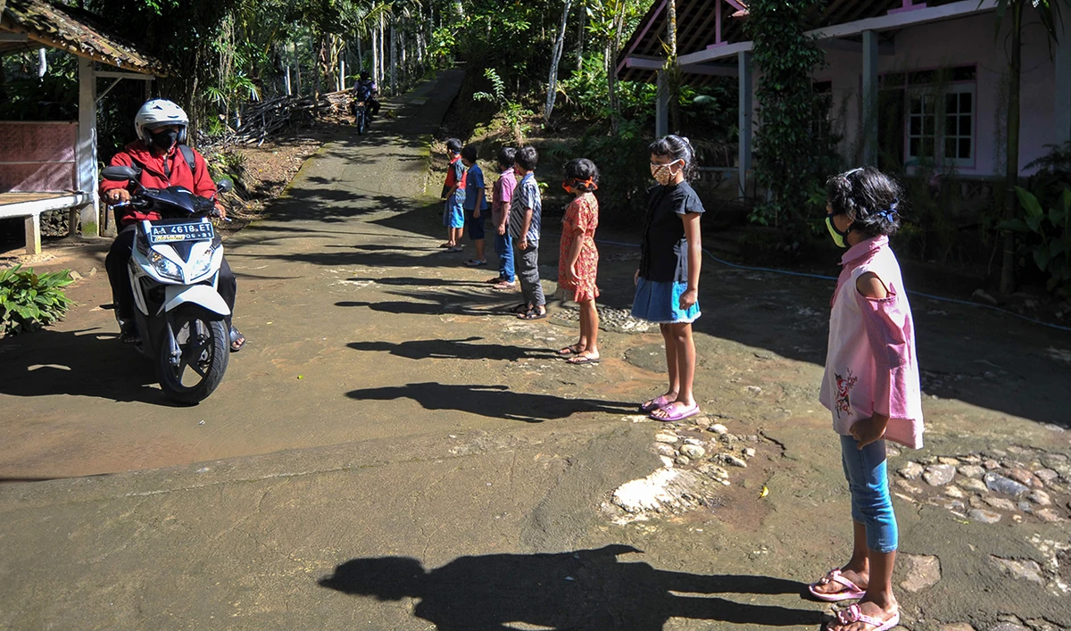 This photo taken on May 20, 2020 shows elementary school students (R) greeting their teacher Henrikus Suroto (L) as he arrives to teach them at their homes in Magelang, Central Java, after schools were closed due to the COVID-19 coronavirus outbreak. (AFP)