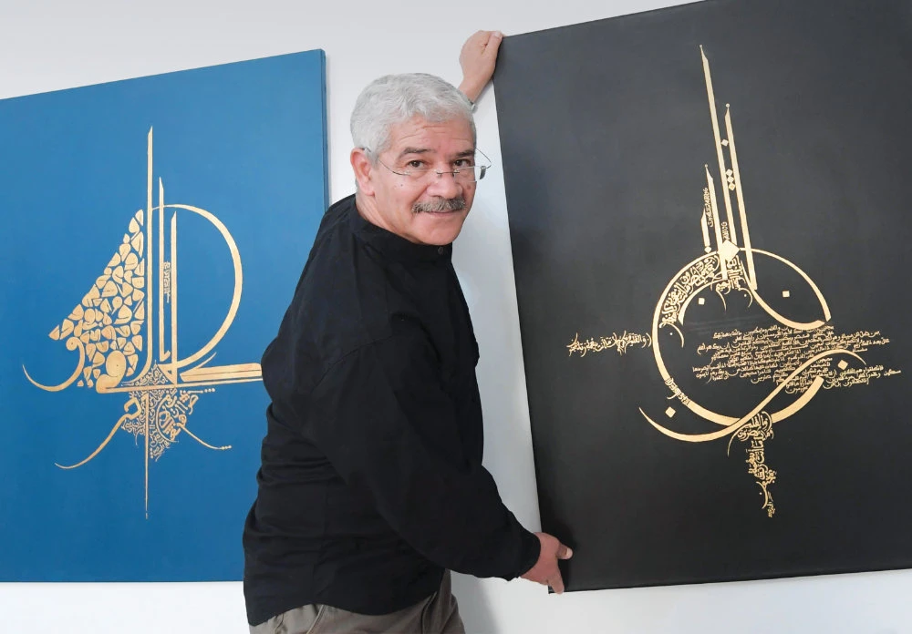 Tunisian calligrapher Omar Jomni stands next to his artwork at his home in the town of Hammam-Lif, about 20 km southeast of Tunis. (AFP)