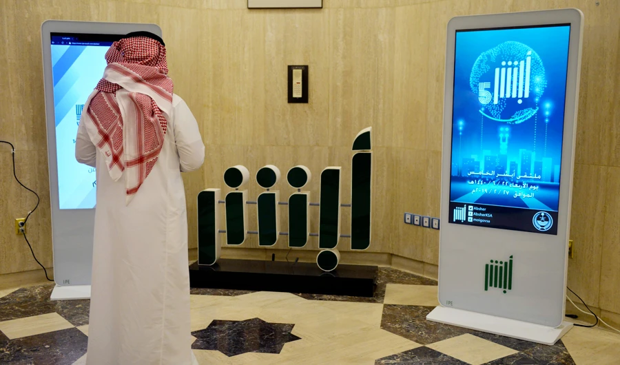 A Saudi Interior Ministry employee stands in front of a screen displaying the Absher mobile app logo at the ministry in Riyadh on February 19, 2019, about the Absher mobile app. (AFP)