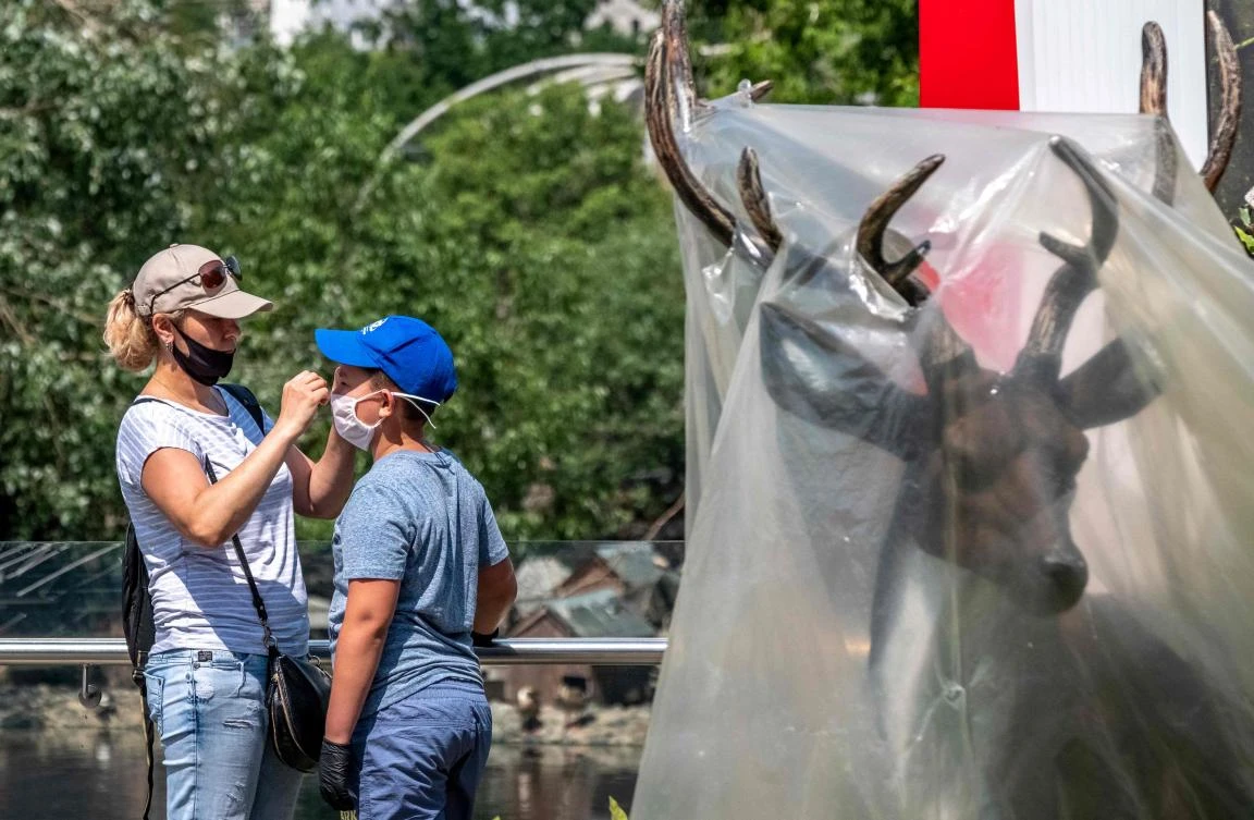 A woman adjusts a face mask on a boy while visiting the Moscow Zoo in Moscow on June 16, 2020 after it reopened as the Russian capital continues to loosen anti-coronavirus restrictions. (AFP)