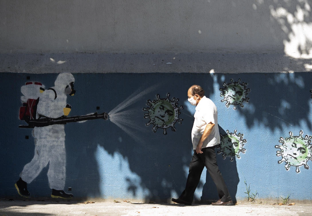 A man walks past a mural representing a worker in protective gear spraying disinfectant on a new coronavirus that has the face of Brazil's President Jair Bolsonaro painted on it, in Rio de Janeiro, Brazil, Monday, June 22, 2020. (AP)
