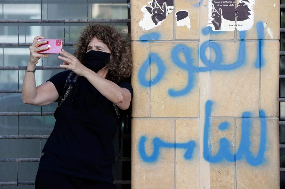 Lebanese director Carol Mansour uses her phone to film while wearing a face mask and standing by graffiti reading in Arabic "power to the people", in Beirut. (File/AFP)