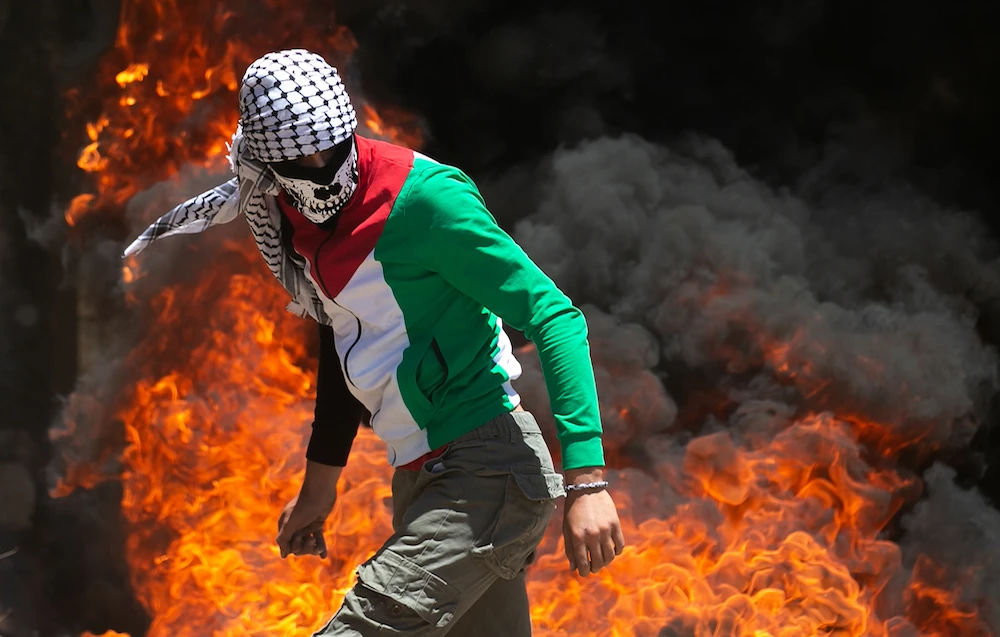 A Palestinian protester walks near burning tires during clashes with Israeli forces during a demonstration in the village of Kfar Qaddum in the Israeli-occupied West Bank, against the Jewish state's plans to annex part of the territory, on June 12, 2020. (AFP/File Photo)