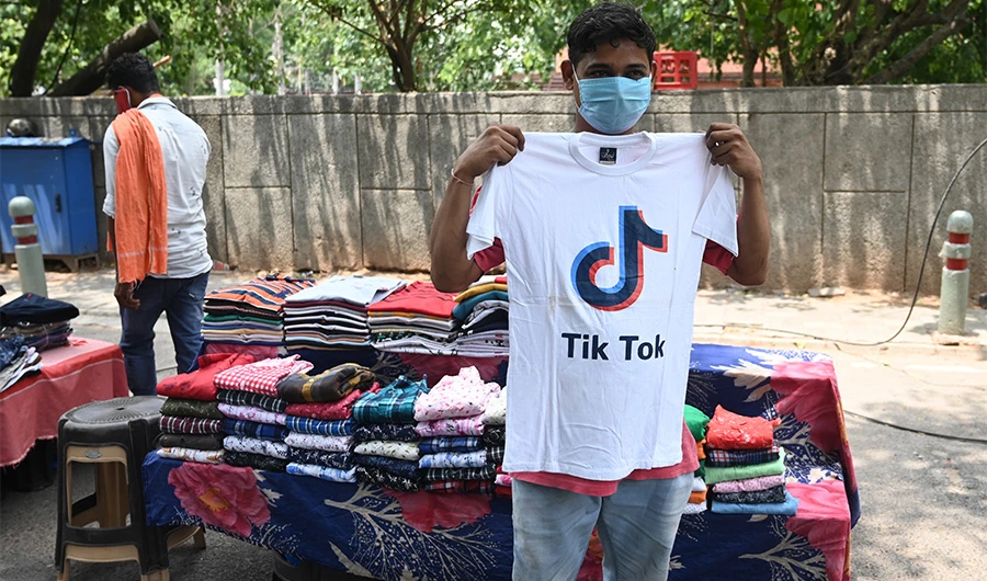 A garment street vendor poses for a picture in front of his stall with a t-shirt with the logo of the social media video-sharing application Tik Tok in New Delhi on June 30, 2020. (AFP)