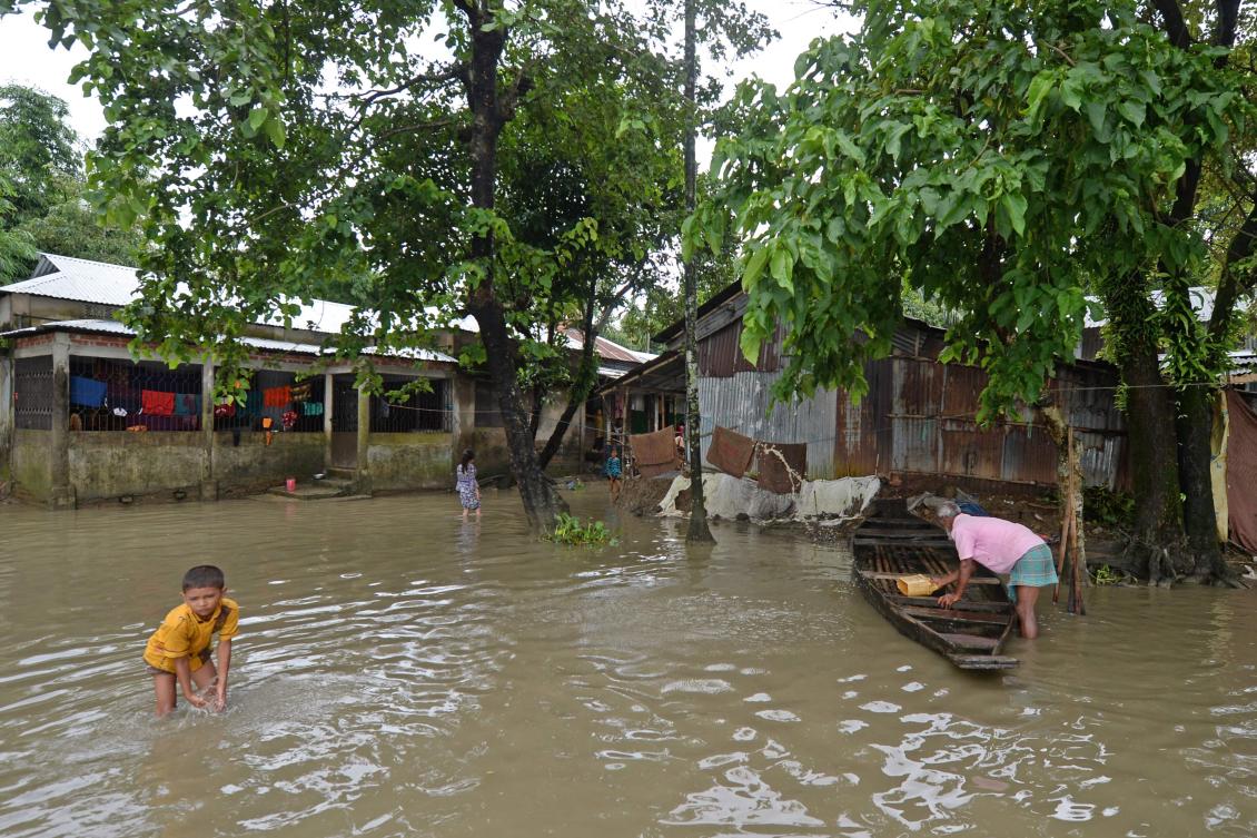 A man works on a boat as a boy walks through flood waters in Sunamgong on July 15, 2020. Almost four million people have been hit by monsoon floods in South Asia, officials said on July 14, with a third of Bangladesh already underwater from some of the heaviest rains in a decade. / AFP / Munir Uz zaman