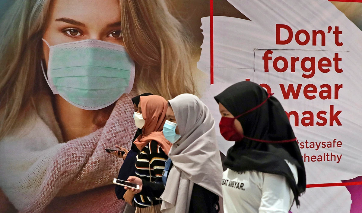 Women wearing protective face masks pass an advertisement promoting awareness of the coronavirus outbreak at a shopping mall in Jakarta, Indonesia, Wednesday, July 1, 2020. (AP)