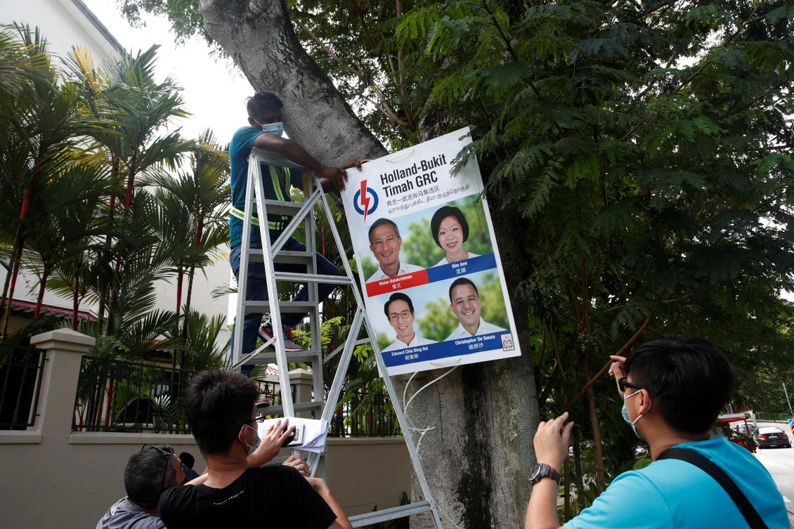 Above, workers hang an electoral poster on a tree at a neighborhood ahead of the general election in Singapore on June 30, 2020. (Reuters)