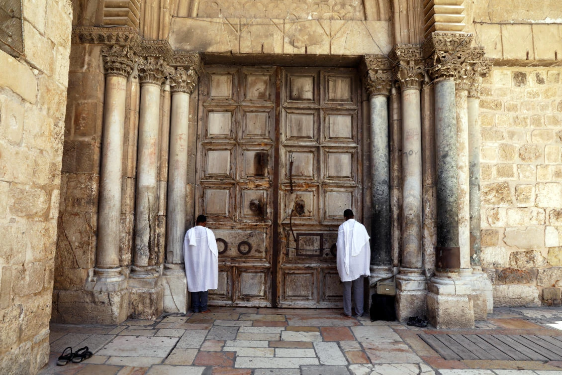 Worshippers pray next to the closed doors of the Church of the Holy Sepulchre, amid the spread of COVID-19, in Jerusalem’s Old City, July 10, 2020. (Reuters)