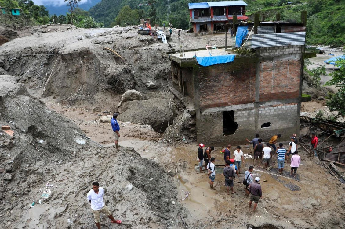 Residents and rescue workers inspect the area outside a house damaged by a landslide and the swell of the Thado-Koshi river due to heavy rains in Jambu village of Sindhupalchok district, some 80 kms northeast of Kathmandu on July 9, 2020. Two people died and several others have gone missing, local media reported. (AFP)