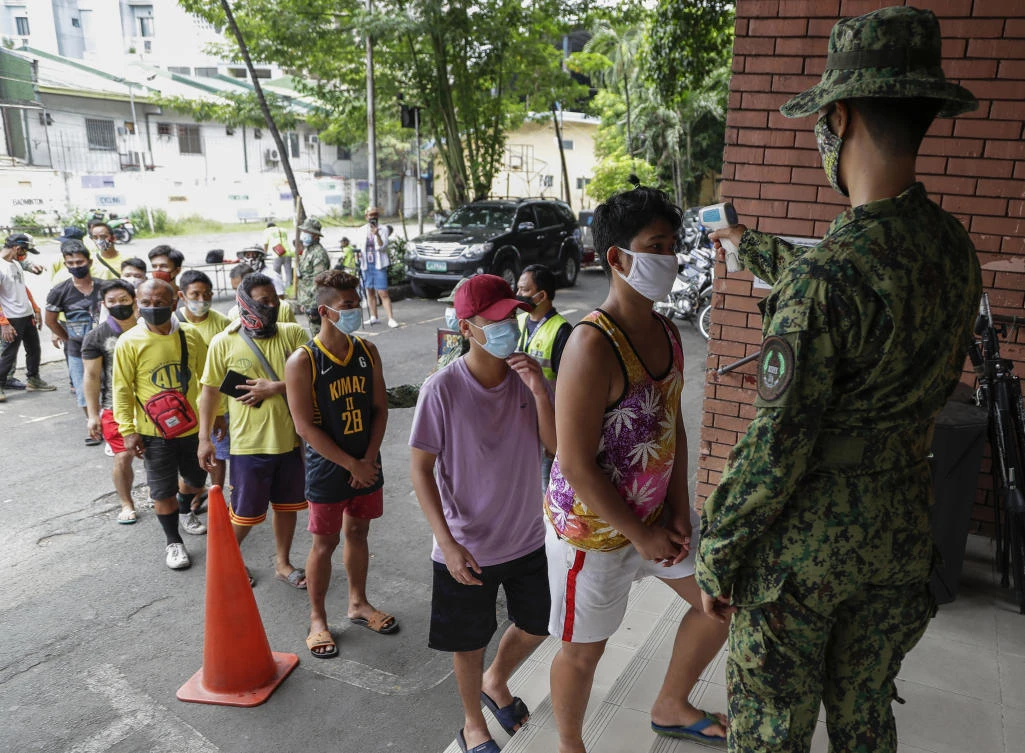 Men who were arrested for violating quarantine health protocols have their temperatures checked at the Amoranto Sports Complex in Manila, Philippines on Wednesday, July 8, 2020. (AP)