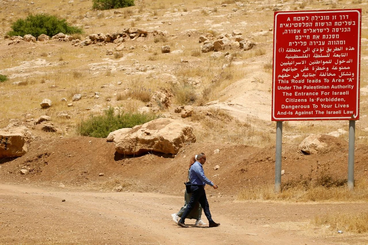Palestinians walk past a sign with information on Area A in the Jordan Valley, in the Israeli-occupied West Bank, June 13, 2020. (Reuters)