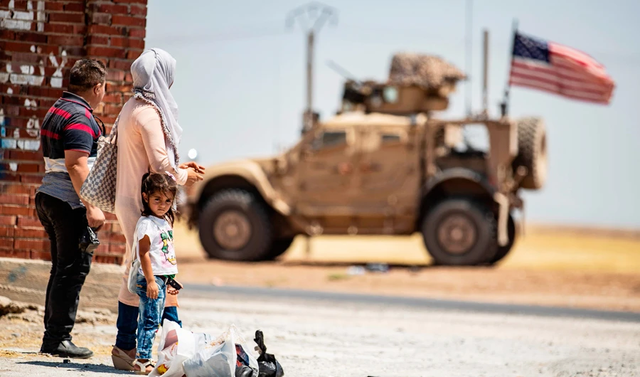 A family stands across a US military vehicle parked on the outskirts of Rumaylan in Syria’s northeastern Hasakeh province. (AFP)