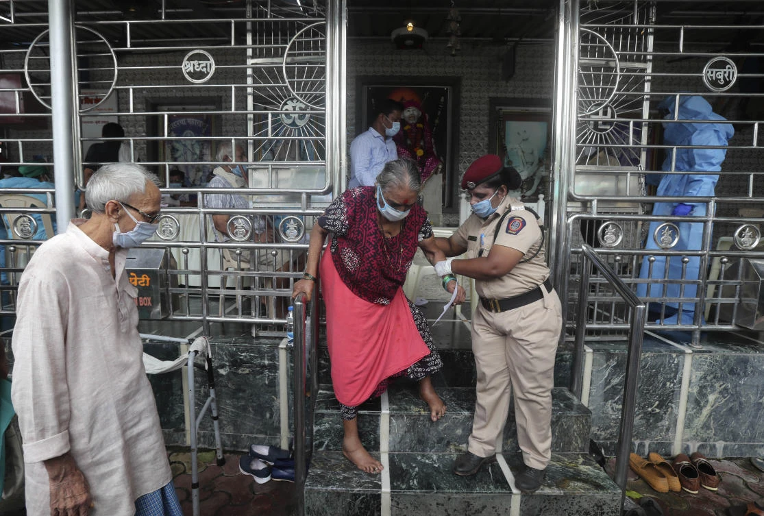 An elderly woman walks down a flight of stairs, helped by a policewoman, after she gave her swab sample, at a temple in Mumbai, India, Saturday, July 18, 2020. (AP)