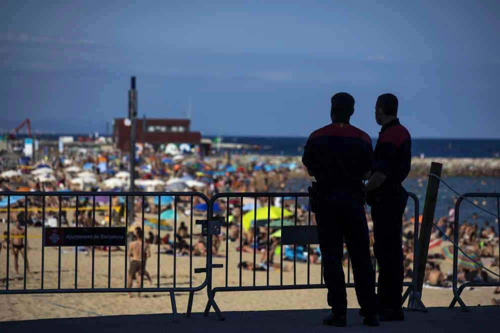 Police officers guard a barrier to stop people entering the beach, in Barcelona, Spain, onJuly 18, 2020. Police in Barcelona are closing access to a large area of the city's beaches due to the excess of sunbathers who decided to ignore the urgings of authorities to stay at home amid a resurgence of the coronavirus. (AP Photo/Emilio Morenatti)