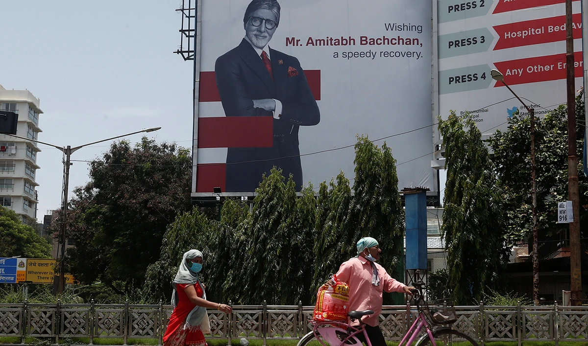 People wearing protective masks walk in front of a hoarding of Bollywood actor Amitabh Bachchan wishing him a speedy recovery in Mumbai, India, July 19, 2020. (Reuters).