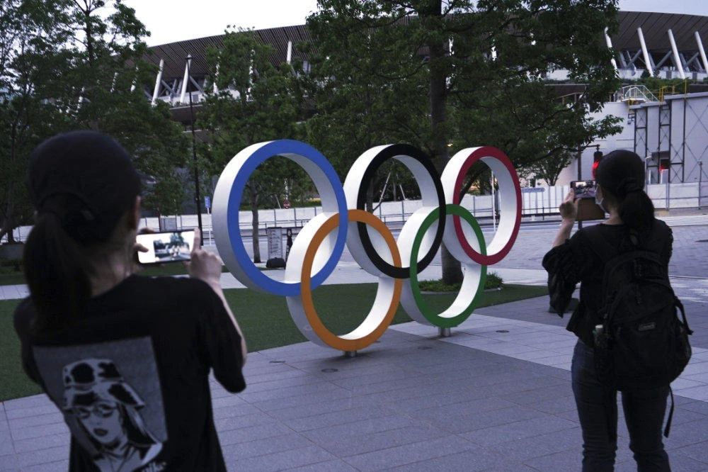 Women take photos of the Olympic rings in front of the New National Stadium on July 22, 2020, in Tokyo. (AP Photo/Eugene Hoshiko)
