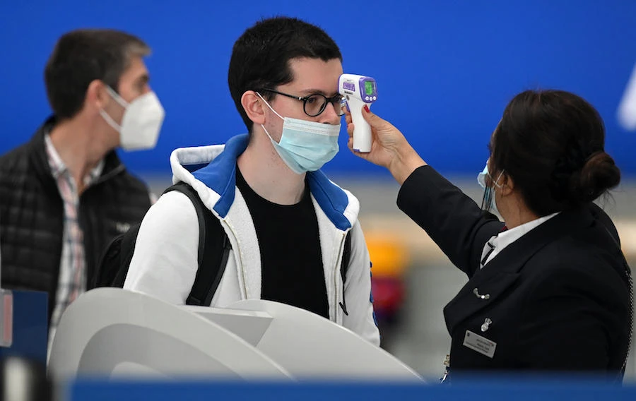 Passengers wearing face masks or covering due to the COVID-19 pandemic, have their temperature taken as they queue at a British Airways check-in desk at Heathrow airport, west London, on July 10, 2020. (AFP)